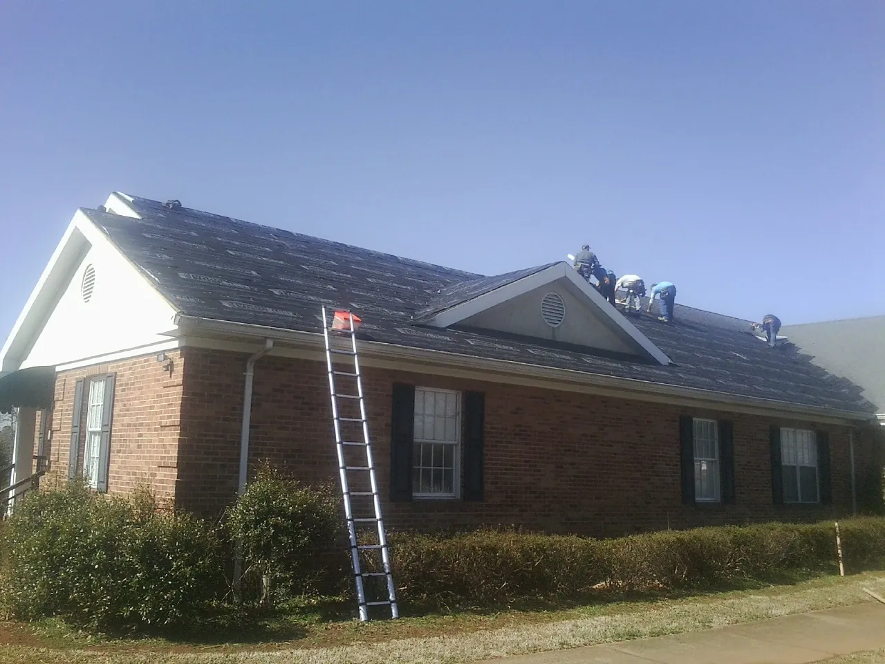 Crew tearing shingles off a brick ranch roof with a ladder set — Metal Roof Repair work by our crew in Palisades