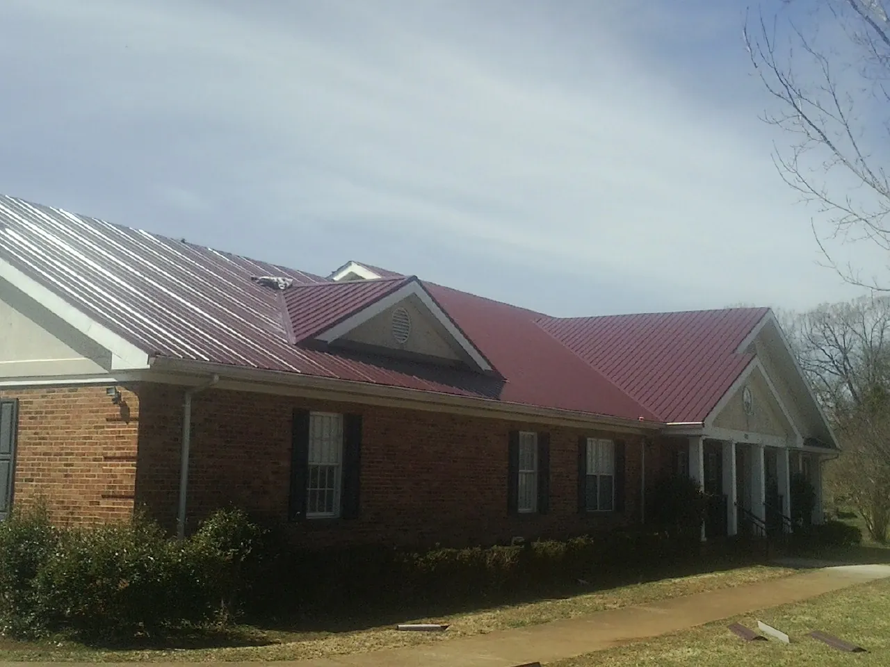 Red metal roof with gabled entries on a long brick building, from a Hail Damage Roof Repair job in Palisades
